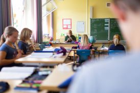 Lehrerin sitzt am Pult und spielt Blockflöte