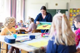 Schülerinnen und Schüler im Kunstunterricht. Lehrerin zeigt ihnen etwas an einem gemalten Bild.